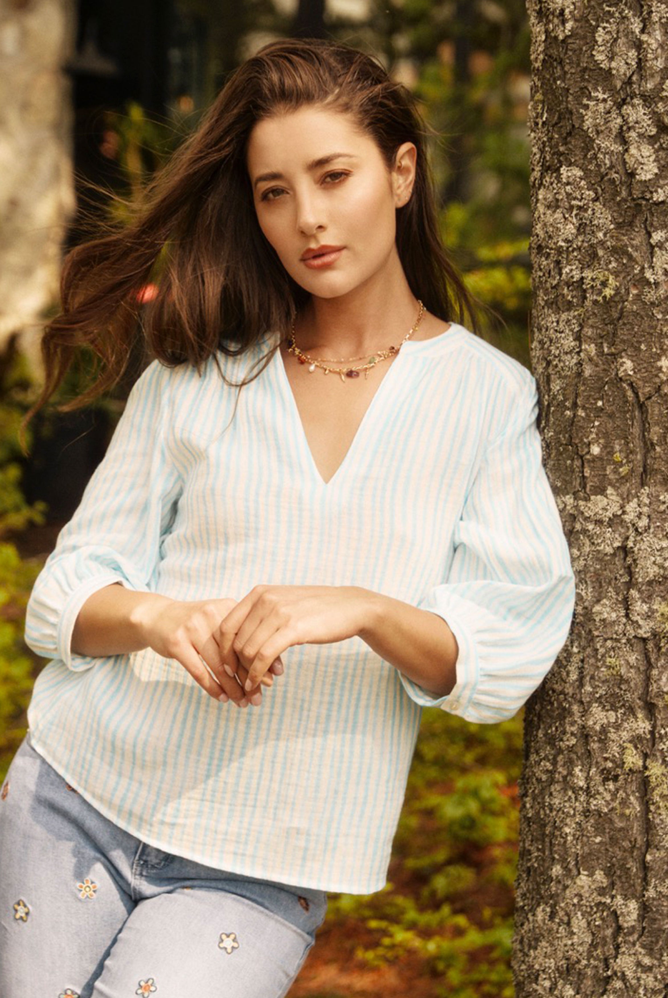 Model leaning against tree in light blue striped blouse, showcasing casual elegance by French Dressing Jeans (FDJ)