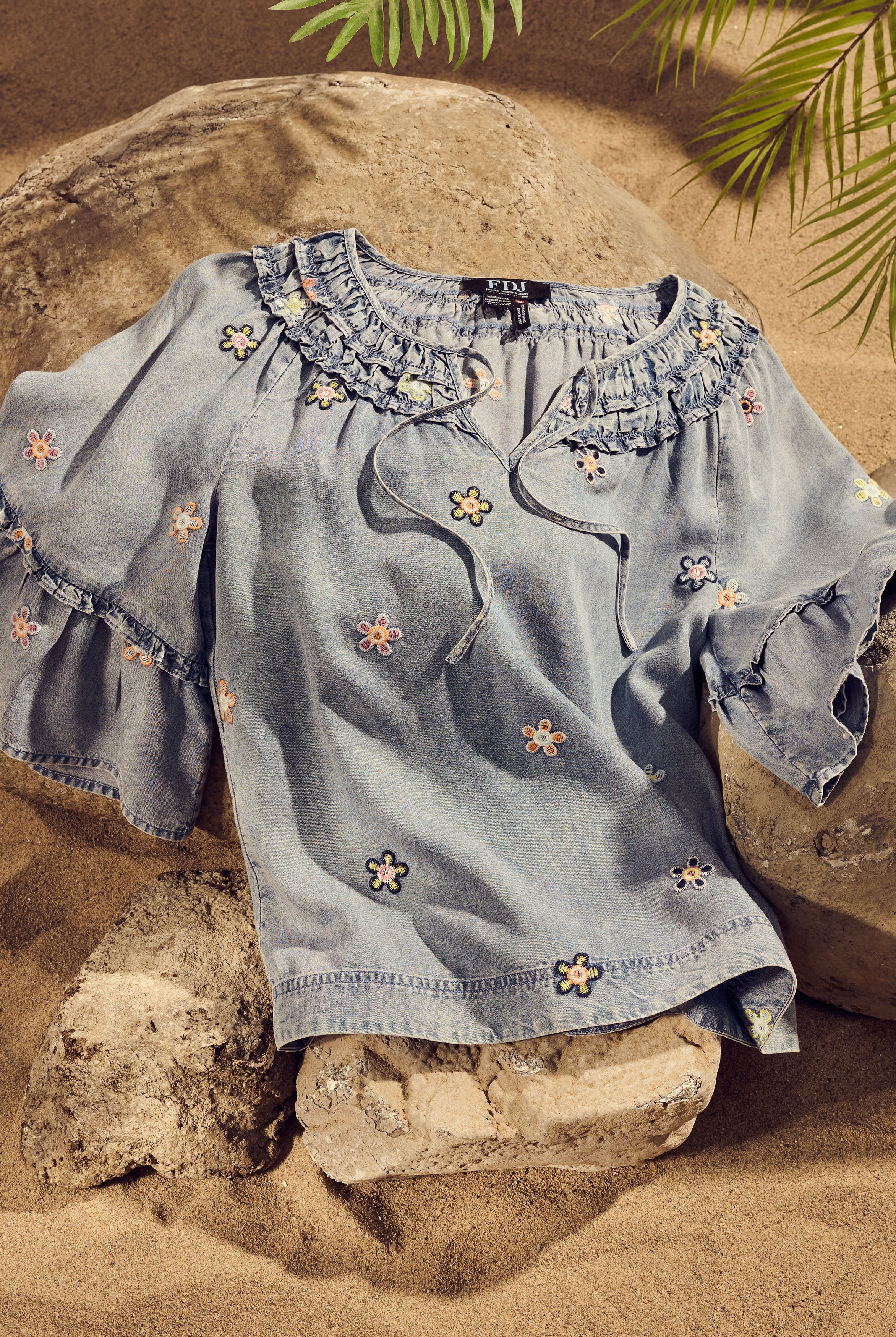 Denim top with floral embroidery and ruffled neckline on rocks by French Dressing Jeans (FDJ)