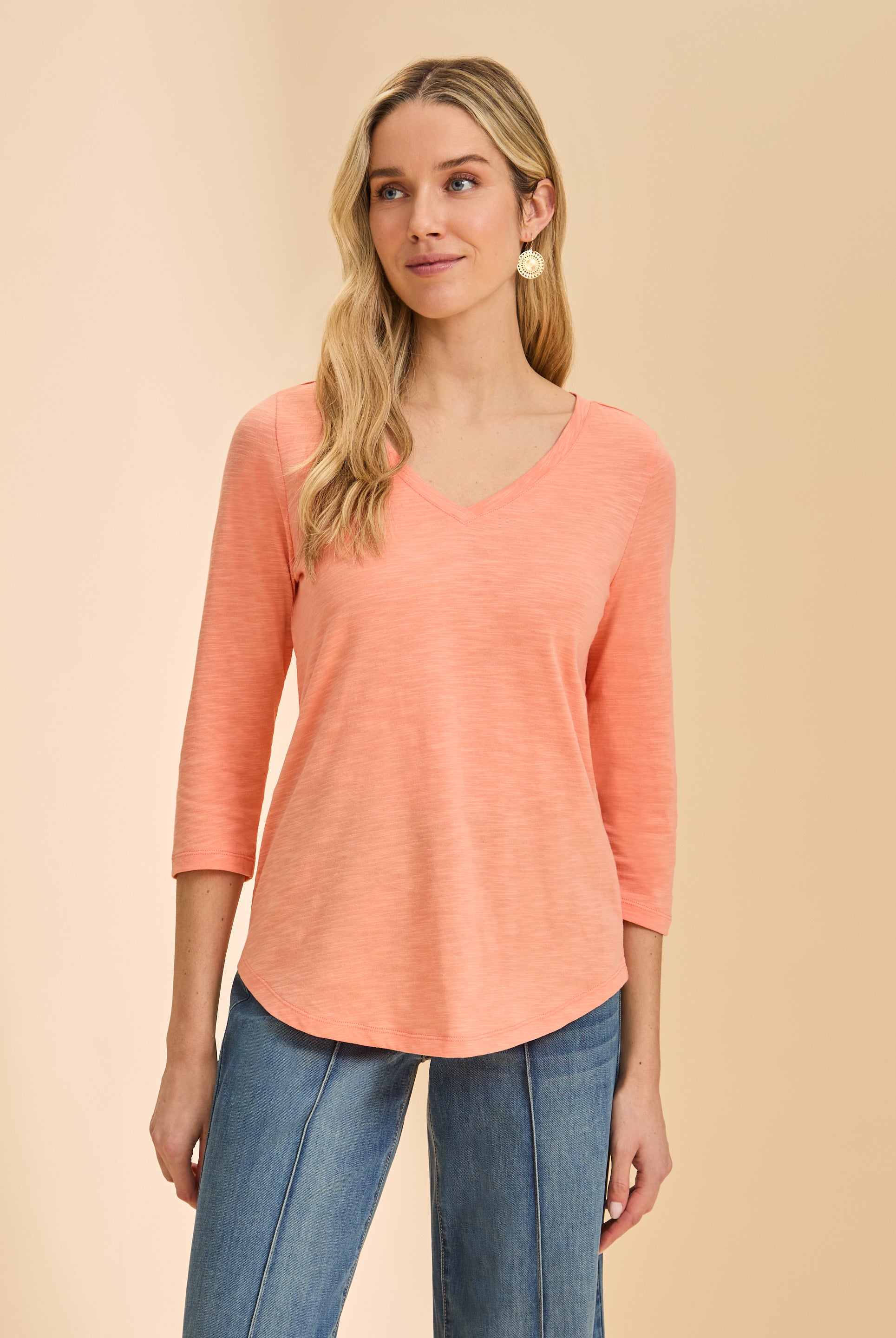 Front view of coral V-neck 3/4 sleeve top with a curved hem paired with denim by French Dressing Jeans (FDJ)
